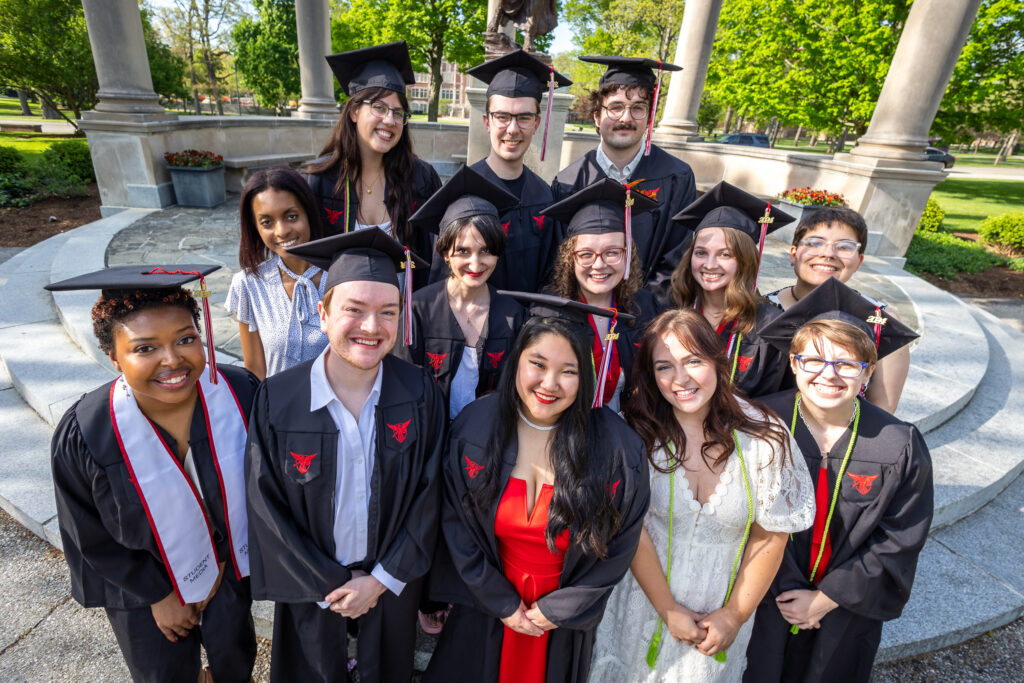 13 Digital Corps students in caps and gowns pose for a picture together 