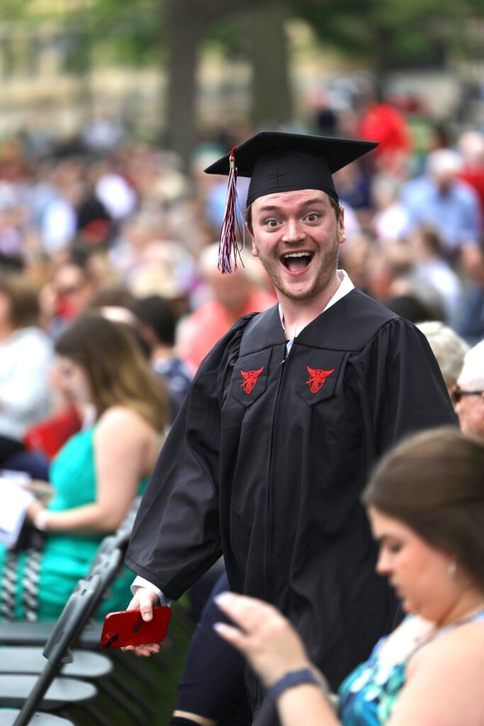 Graduating student in cap and gown smiles excitedly at the camera walking up to receive his diploma.