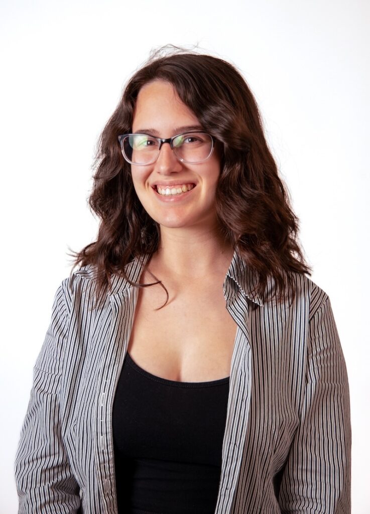 Digital Corps Specialist, Luci Bluto, smiles for the camera. She has dark, shoulder-length hair and glasses.